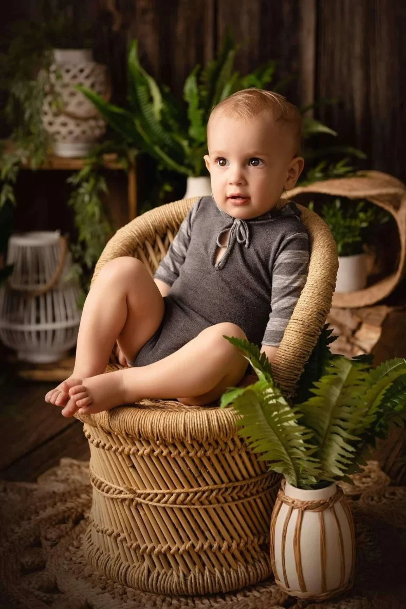Tout-petit assis dans un panier, dans un décor de bois et de plantes