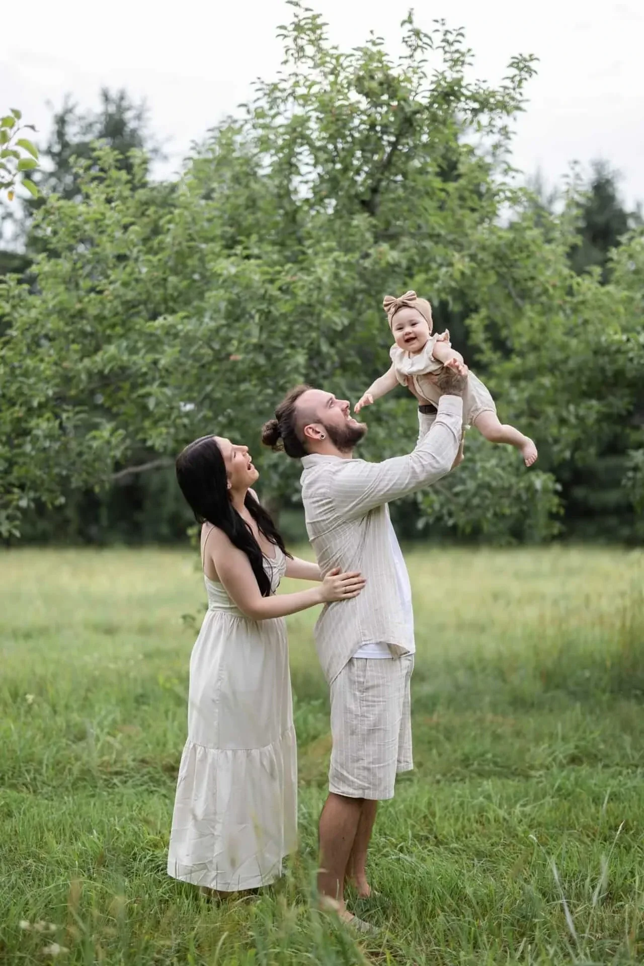 Des parents soulèvent leur bébé dans un verger, au soleil couchant