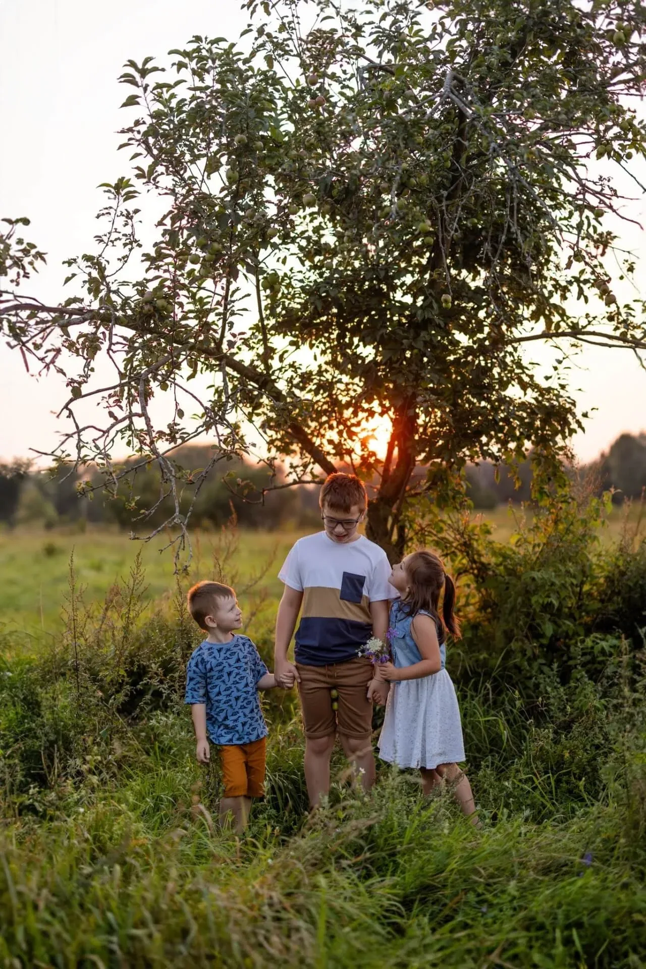 Trois enfants réunis sous un pommier au coucher du soleil