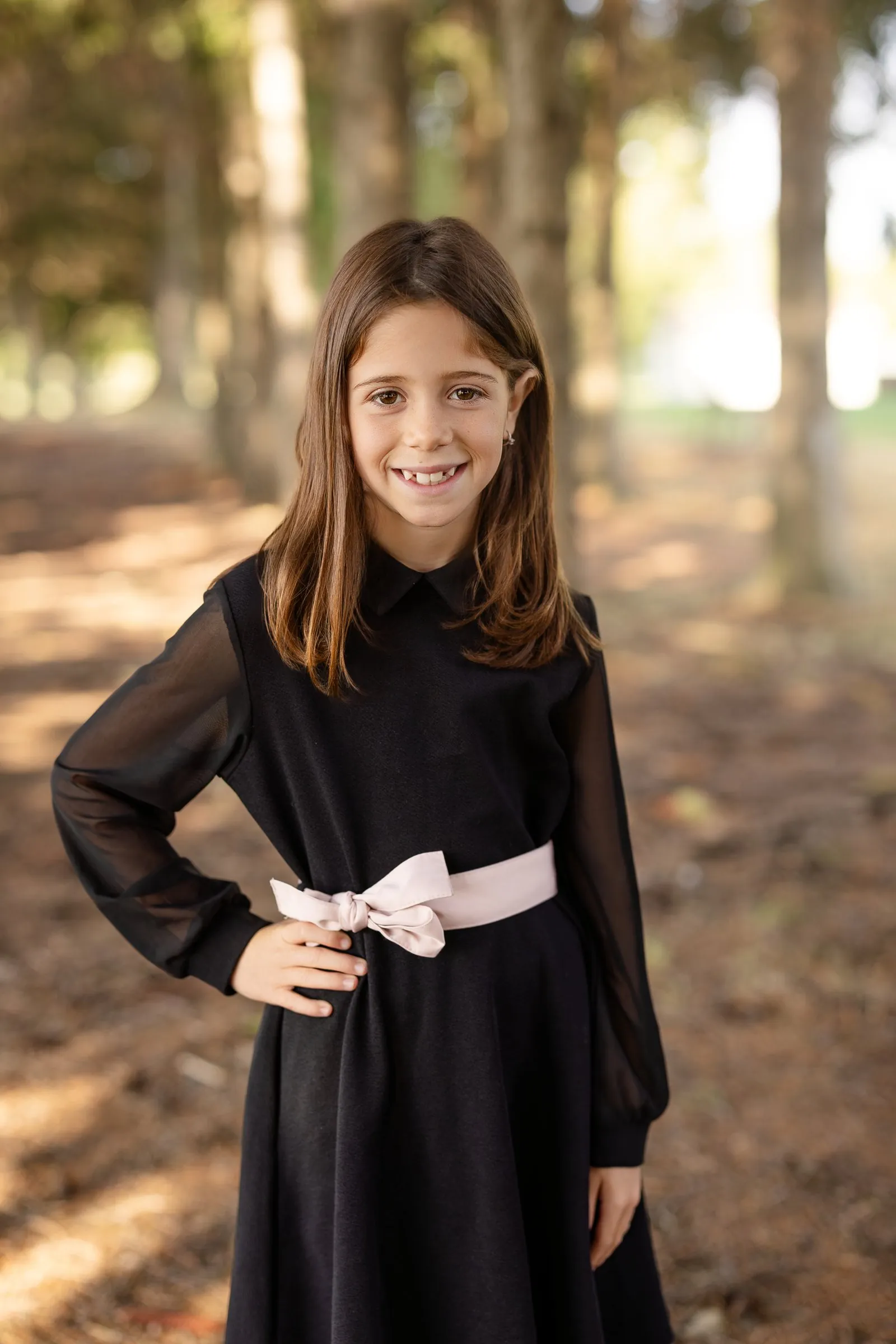 Portrait scolaire d’une élève en robe noire à nœud rose, dans un sous-bois